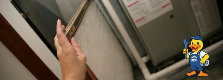 Hand removing a dirty HVAC air filter from a residential furnace for routine maintenance and improved indoor air quality.
